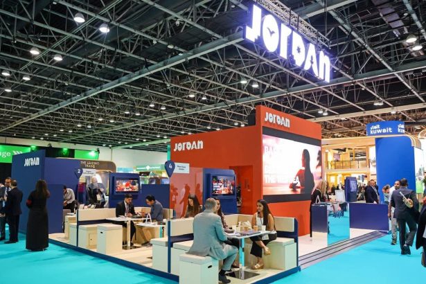 جناح هيئة تنشيط السياحة الأردنية المشارك في معرض سياحي دولي يضم أماكن جلوس وزواراً مع شعار Jordan المضيء.