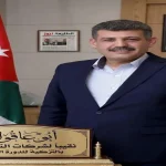 الدكتور ضيف الله أبو عاقولة نقيب أصحاب شركات التخليص ونقل البضائع في الأردن يبتسم أمام العلم الأردني.