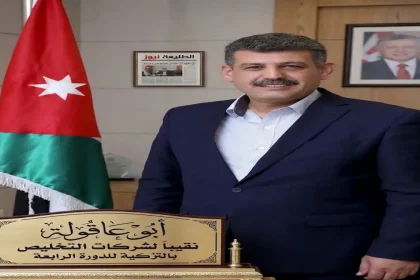الدكتور ضيف الله أبو عاقولة نقيب أصحاب شركات التخليص ونقل البضائع في الأردن يبتسم أمام العلم الأردني.