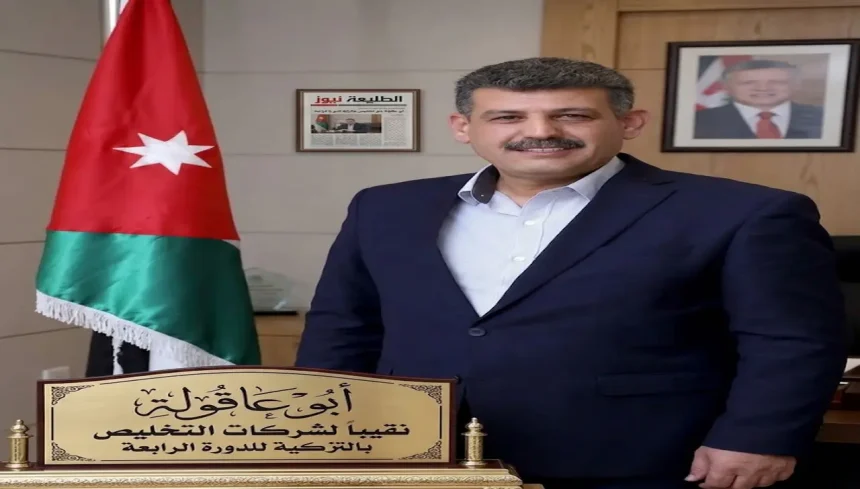 الدكتور ضيف الله أبو عاقولة نقيب أصحاب شركات التخليص ونقل البضائع في الأردن يبتسم أمام العلم الأردني.
