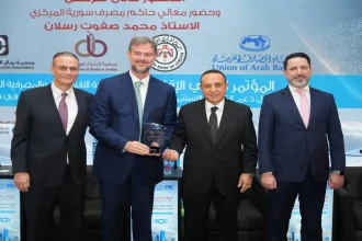 ممثلو البنك الأردني الكويتي يحملون درع التكريم في مؤتمر دعم الاستثمار في سوريا بحضور مسؤولين.