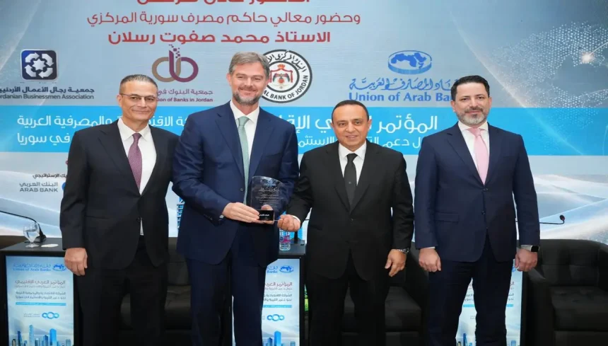 ممثلو البنك الأردني الكويتي يحملون درع التكريم في مؤتمر دعم الاستثمار في سوريا بحضور مسؤولين.