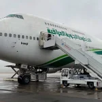 طائرة الخطوط الجوية العراقية تجثم على أرض المطار متصلة بسلم الركاب وسط أجواء غائمة.