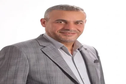 صورة لـ عماد عبدالقادر عمرو ببدلة سوداء يقف أمام طاولة عليها لوحة باسمه وأعلام أردنية وصناديق اقتراع، خلف خلفية مكتوب عليها "انتخابات الغرف التجارية والصناعية الأردنية" وشعار "الطليعة نيوز".