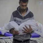 أب فلسطيني يحمل جثمان طفله ملفوفاً بالكفن الأبيض ضمن شهداء غزة بعد الهدنة في مستشفى مكتظ بالجرحى