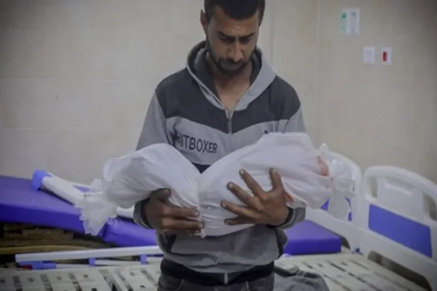 أب فلسطيني يحمل جثمان طفله ملفوفاً بالكفن الأبيض ضمن شهداء غزة بعد الهدنة في مستشفى مكتظ بالجرحى