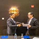 لحظة توقيع اتفاقية شراكة وتبادل المستندات بين رجلين في قاعة اجتماعات رسمية.