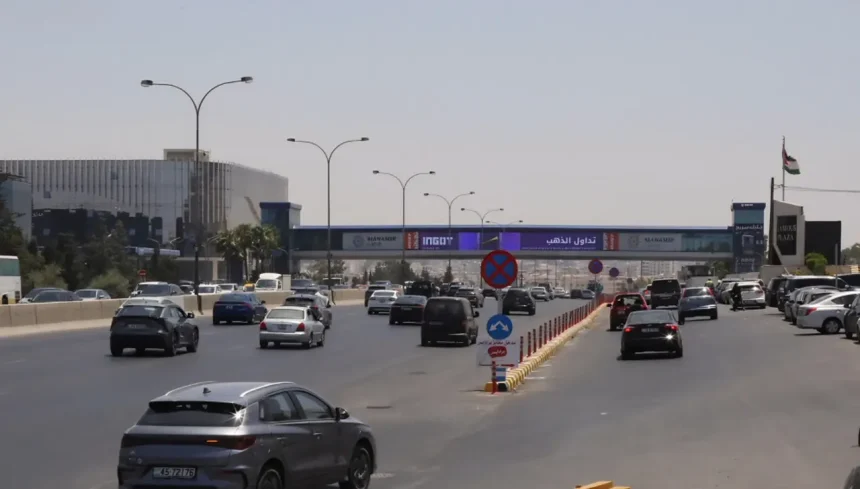 سيارات تسير في طريق عمان الرئيسي بالقرب من جسر المشاة واللوحات الإعلانية في الأردن