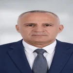 صورة شخصية رسمية ليونس العبادلة يرتدي بدلة كحلية وربطة عنق رمادية خلفية رمادية فاتحة