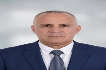 صورة شخصية رسمية ليونس العبادلة يرتدي بدلة كحلية وربطة عنق رمادية خلفية رمادية فاتحة